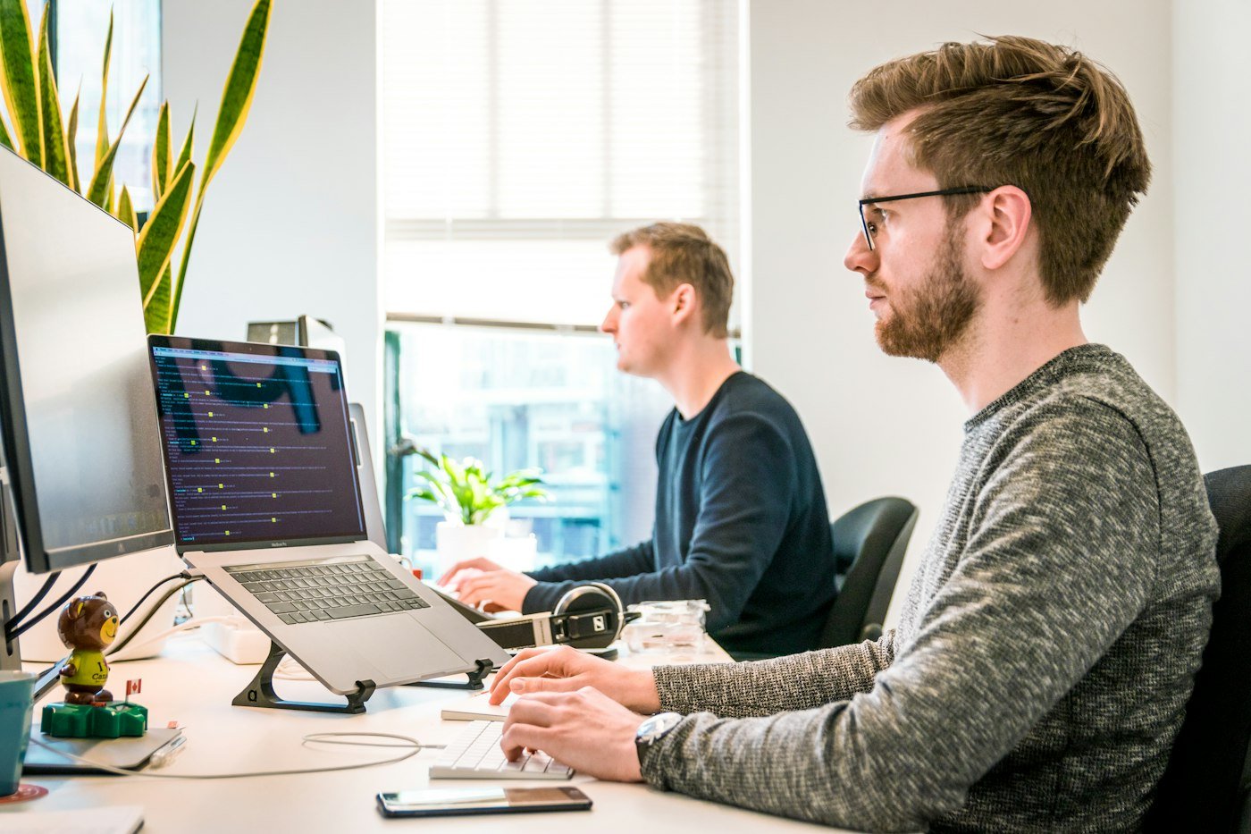 Dwie osoby przy komputerach, jedna przy monitorze, druga przy laptopie